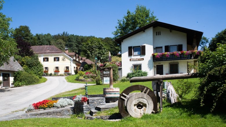 Guest house, © Gästehaus Buchegger, Foto Buchegger A rural guest house with flowers and an old millstone in the foreground.