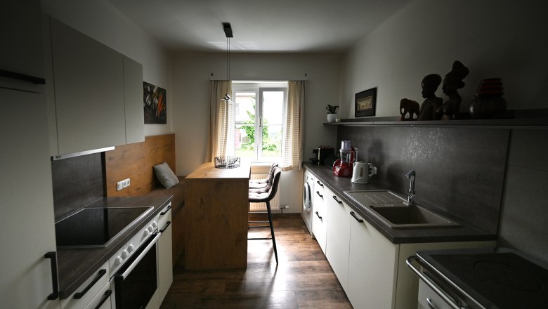 Kitchen, © Christine Kuppelwieser Modern kitchen with wood and metal accents, dining table by the window, kitchen appliances and decorations on shelves.