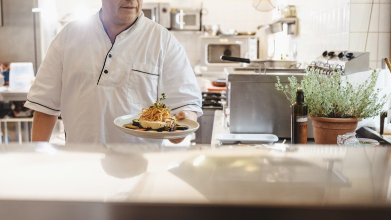 Wine is omnipresent in Georg Kruder's inn, © Niederösterreich Werbung/Michael Reidinger A cook in a restaurant kitchen holds a plate of food in his hand.