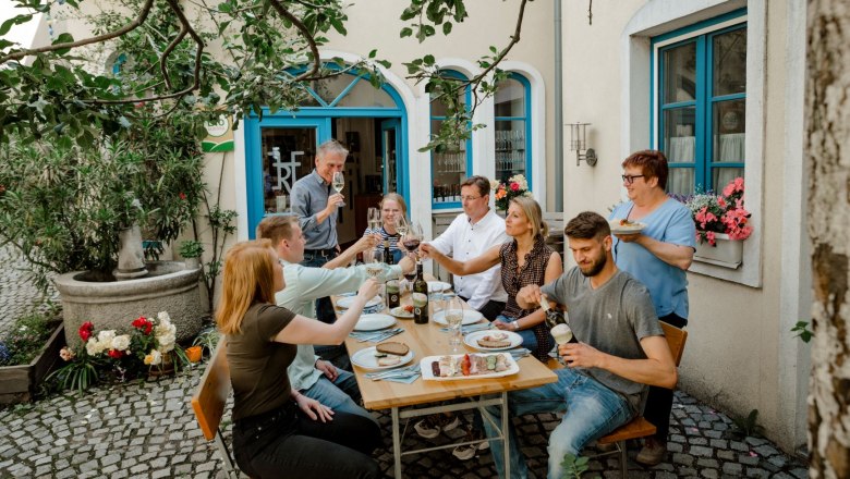 Hofer family, © Astrid Bartl A group of people sit at an outdoor table and toast with drinks.