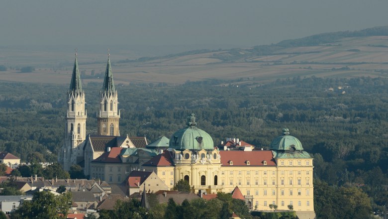 Stift Klosterneuburg, © Stift Klosterneuburg/Michael Zechany Aerial view of Stift Klosterneuburg Abbey with two towers and a dome, surrounded by forest and fields.