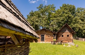 Celtic village Schwarzenbach, © Wiener Alpen, Christian Kremsl Reconstruction of a Celtic village with wooden huts and a green lawn surrounded by trees.