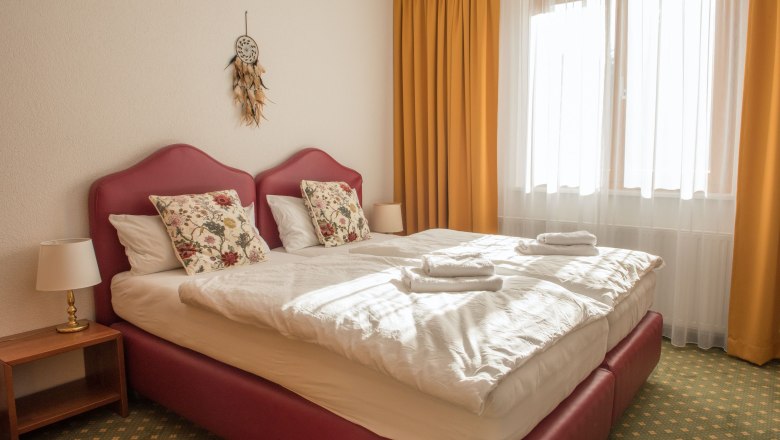 Double room 11, © Dorfschmiede eG A cozy double room with two beds, yellow curtains and a dream catcher on the wall.