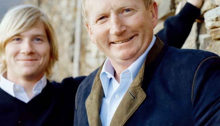 Hirtzberger Franz, © Jellasitz Two men stand in front of a stone wall, one smiling into the camera.