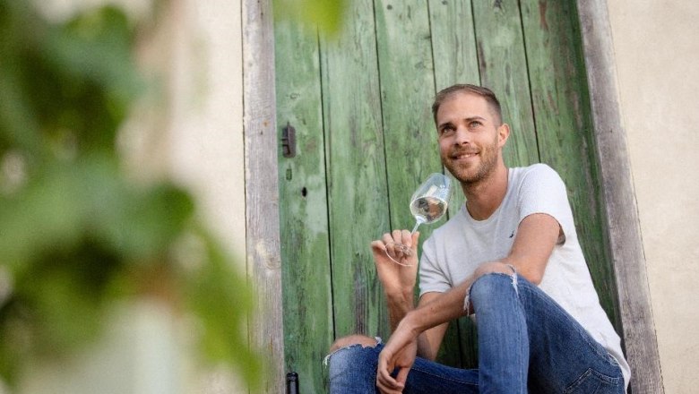 Bernhard Winter, © Astrid Bartl A man is sitting in front of a green wooden door, holding a wine glass in his hand.