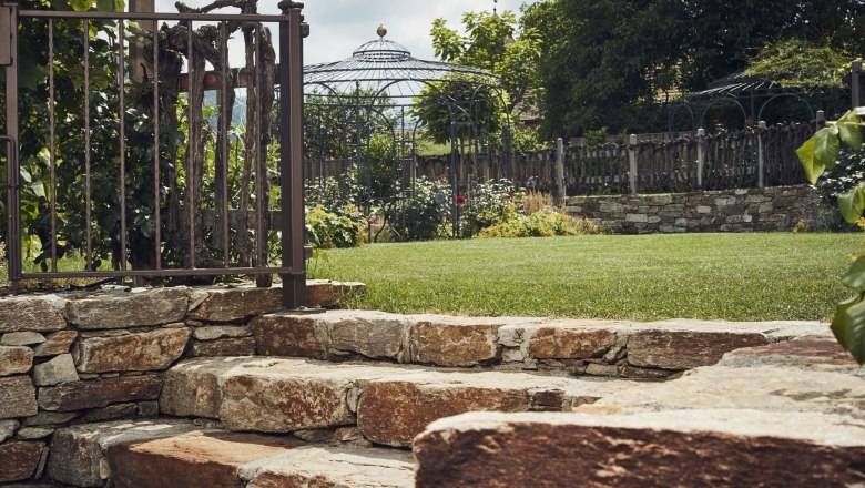 Naturally romantic garden, © Niederösterreich Werbung/Andreas Hofer Stone steps in the garden with metal fence and pavilion in the background.