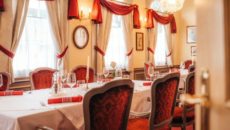 Fine ambience with gourmet menus, © Niederösterreich Werbung/Daniela Führer Elegant restaurant with table setting, red chairs and chandelier.