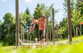 St. Corona motor skills park, © Wexl Arena St. Corona am Wechsel A woman holds a child by the hands in an outdoor play area with wooden posts and ropes.