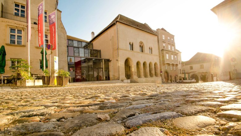 Exterior view of Restaurant Gozzo by Late, © Charly Teuschl Exterior view of a historic building with a modern glass façade and cobblestones in the foreground.