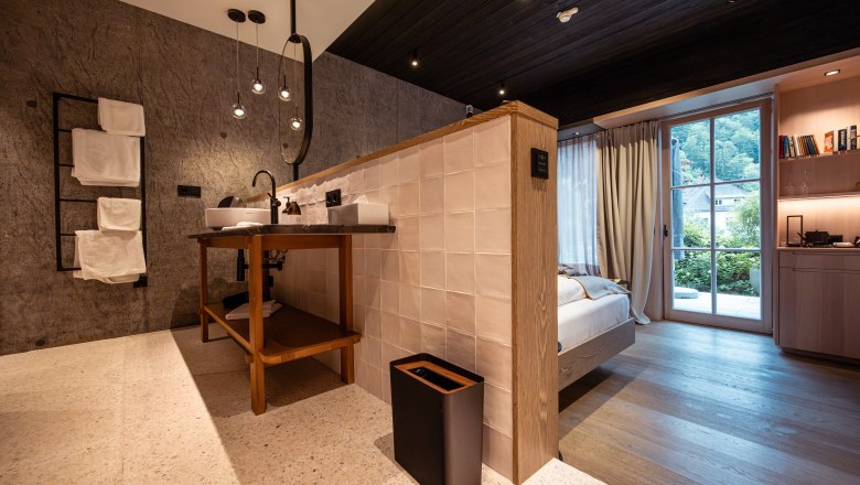 Refugium Lunz, © Niederösterreich Werbung / Maximilian Pawlikowsky Modern hotel room with open bathroom, wooden floor and large windows with a view of the greenery.