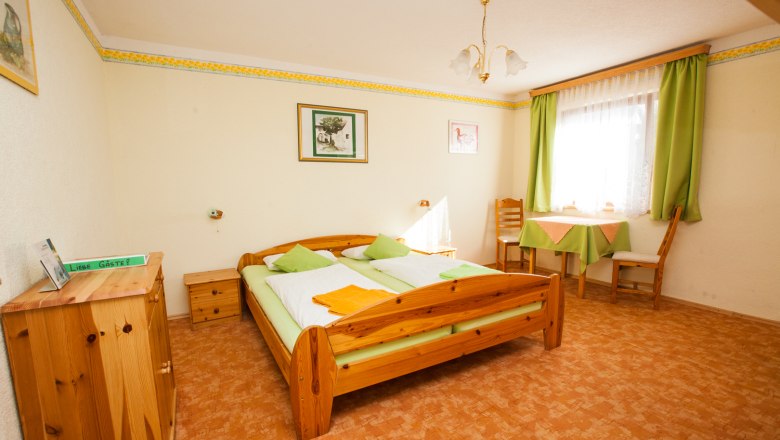 Guest room, © Schneider Cozy guest room with wooden furniture, double bed, table and chairs, green curtains and decoration.