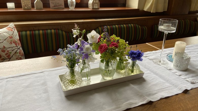 Beautifully decorated tables, © Wiener Alpen A table with a white tablecloth, decorated with small vases full of colorful flowers and candle holders.