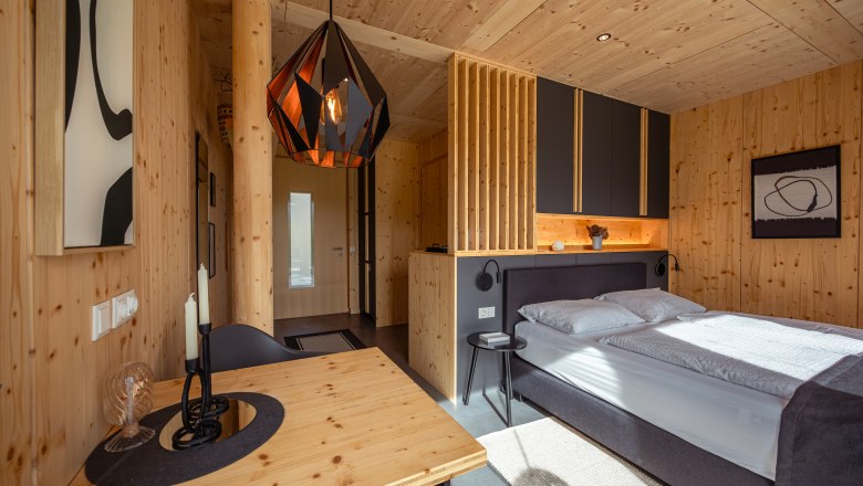 roo'n, © Niederösterreich Werbung / Maximilian Pawlikowsky Modern bedroom with wooden walls, a bed, a table and a geometric hanging lamp.