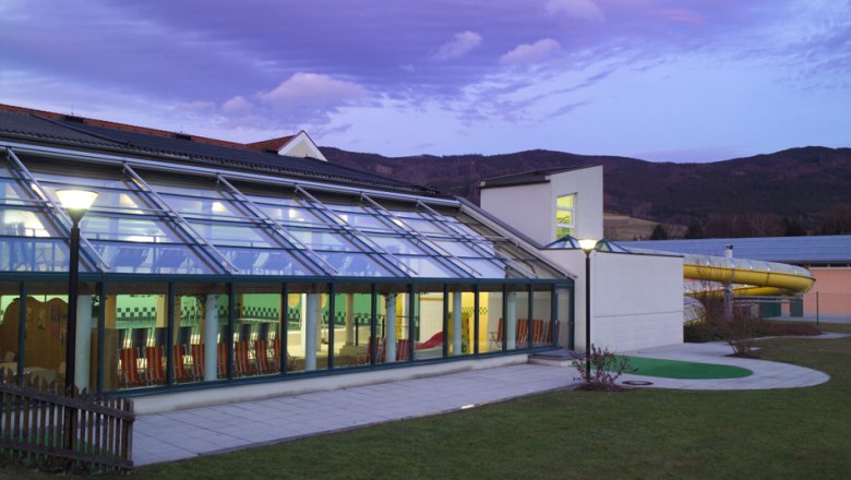 Indoor swimming pool Yspertal, © Hallenbad Yspertal Exterior view of the Yspertal indoor pool at dusk with glass façade and slide.