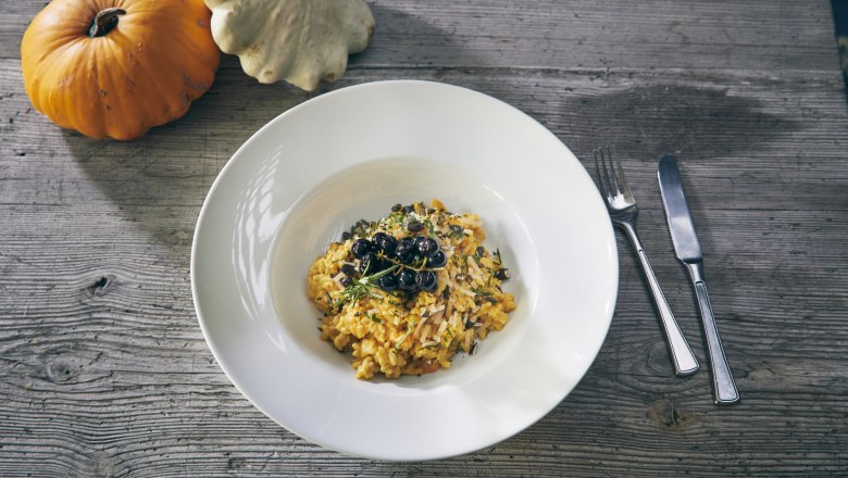 Pumpkin risotto, © Niederösterreich Werbung/Andreas Hofer A plate of pumpkin risotto with herbs and berries, next to two pumpkins on a wooden table.