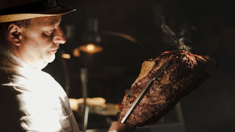1st Carnuntum barbecue school, © Niederösterreich Werbung/Michael Reidinger A man in a white shirt holds a large, grilled piece of meat with a knife.
