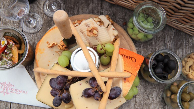 Cheese basket, © Schloss Wartholz - Nusterer Cheese platter with grapes, nuts and breadsticks on a wooden table.