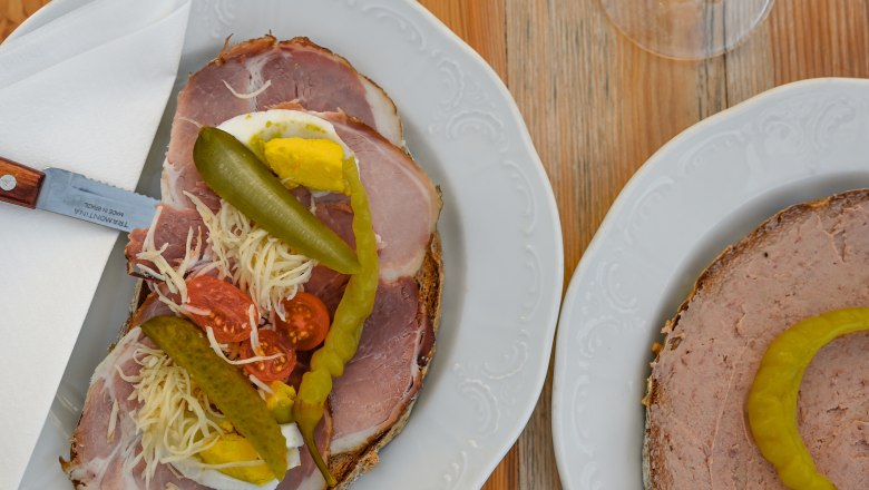 Heurigen snack, © Weinviertel Tourismus GmbH / Lisa Sedlatschek Two plates with sandwiches and two glasses of white wine on a wooden table.