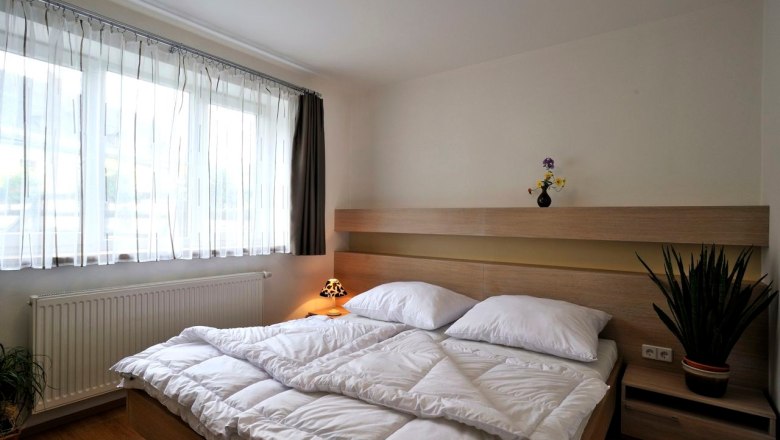 Apartments Lobkowicz, © Ferienwohnungen Lobkowicz Modern bedroom with double bed, light wooden furniture and large windows with white curtains.