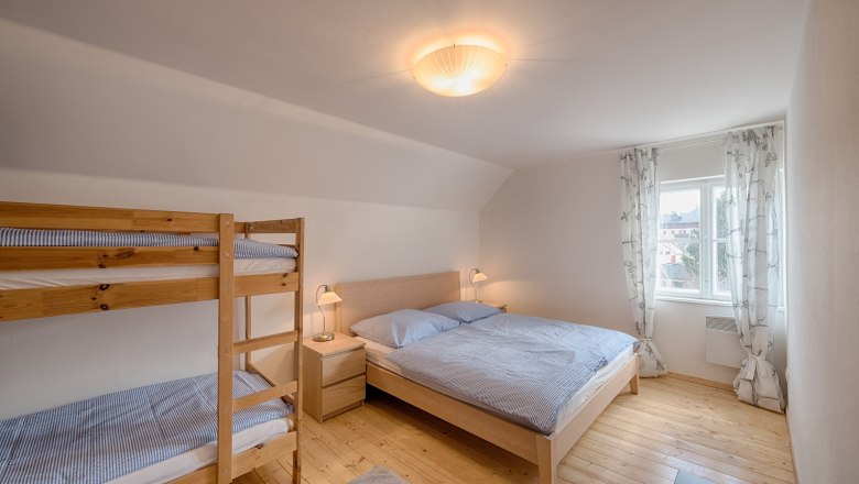 Top 6 - Bedroom, © VP FeWo OG Bright bedroom with double bed and bunk bed, wooden floor and window with curtains.