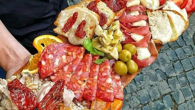 Antipasti, © Andy Edlinger A large wooden platter with various antipasti, including sausage, cheese, olives and dried tomatoes, is held by one person.