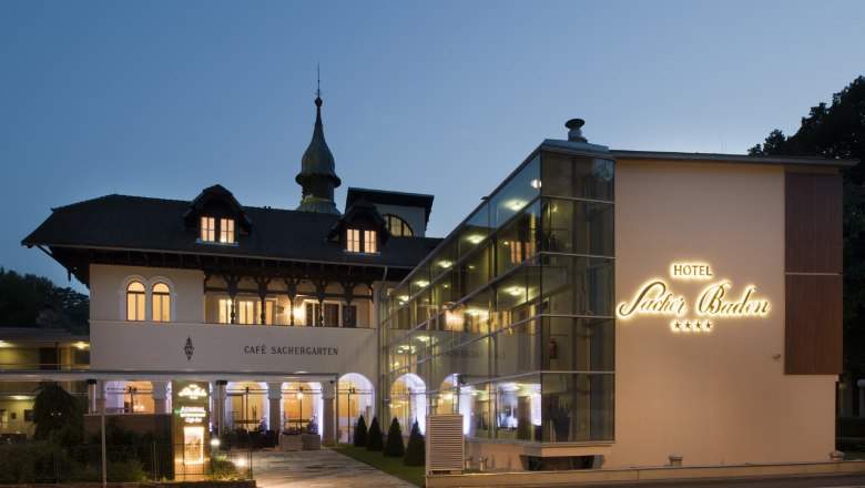 Hotel Sacher Baden, © Hotel Sacher Baden Exterior view of the Hotel Sacher Baden at dusk with illuminated lettering and historic building.