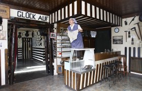 Grünbach Mining Museum, © Wiener Alpen, Foto: Bene Croy Interior view of a mining museum with a person in traditional clothing standing on a counter.