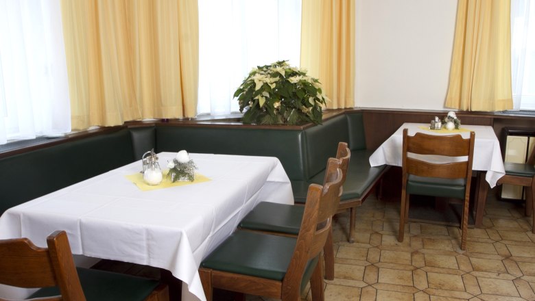 Breakfast room, © Gasthof zur Sonne A breakfast room with laid tables, green upholstered benches and yellow curtains.