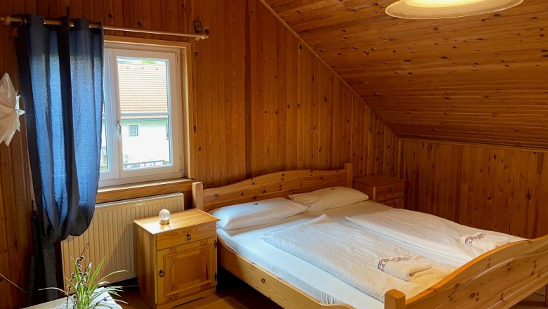Double room, © Wiener Alpen Cozy double room with wood paneling, double bed, window with blue curtains and a plant on the table.