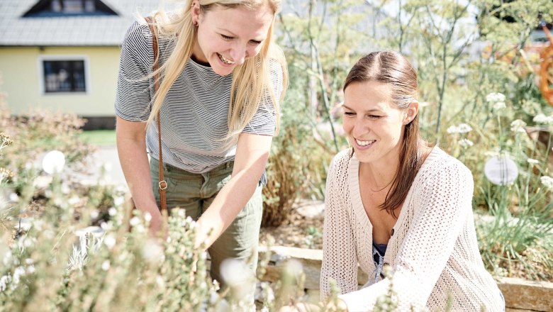 SONNENTOR Girlfriends, © ©SONNENTOR/@nudlholz.at Two women smile and work in a garden with herbs.