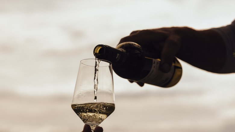 Pouring wine, © Weinviertel Tourismus / Sophie Menegaldo Wine is poured into a glass outdoors, with a landscape in the background.