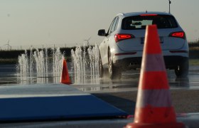 Driving Camp Pachfurth, © Driving Camp Pachfurth A car drives on a wet road with water fountains and traffic cones.