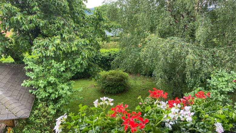 View from the guest balcony, © Wiener Alpen View from the balcony onto a green garden with trees and red and white flowers in the foreground.