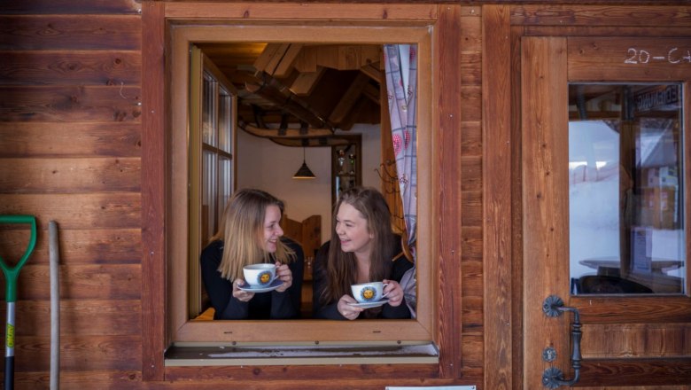 Kirchbochstadl, © Waldviertel Tourismus, Robert Herbst Two women look out of a window of a wooden hut and hold cups in their hands.