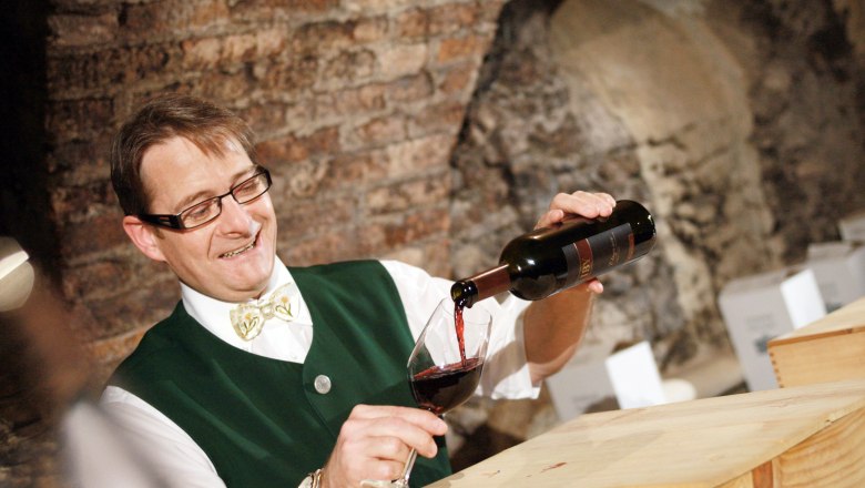 Eisenstraße landlord Martin Teufl, © weinfranz.at A man in traditional dress pours red wine into a glass.