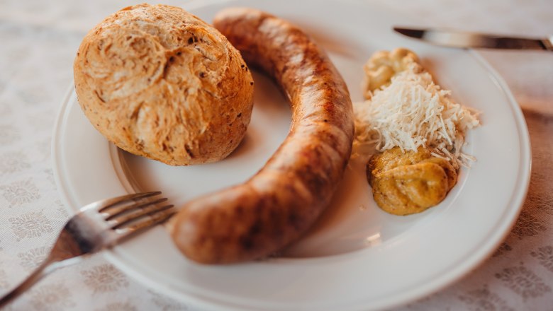 Braumeister sausages with beer grain slices, © Niederösterreich Werbung/Daniela Führer A plate with a bratwurst, a roll, mustard and grated horseradish.