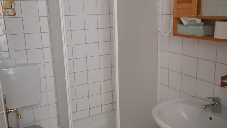 Bathroom, © Karl Buchner A small, white tiled bathroom with shower, toilet and washbasin.