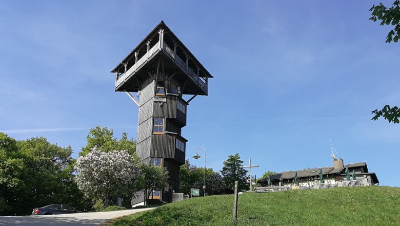 Buchbergwarte with shelter, © Roman Zöchlinger A wooden observation tower next to a building on a hill under a blue sky.