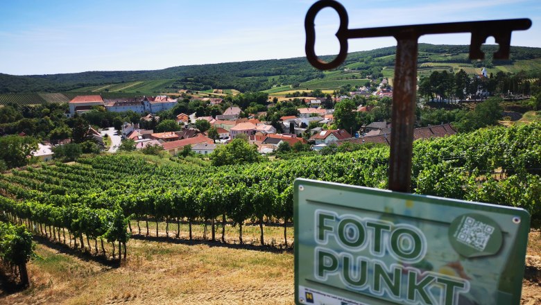 Fantastic photo spot in the Hundschupfen vineyard, © Weinstraße Weinviertel View of a village surrounded by vineyards with a 'photo point' sign in the foreground.