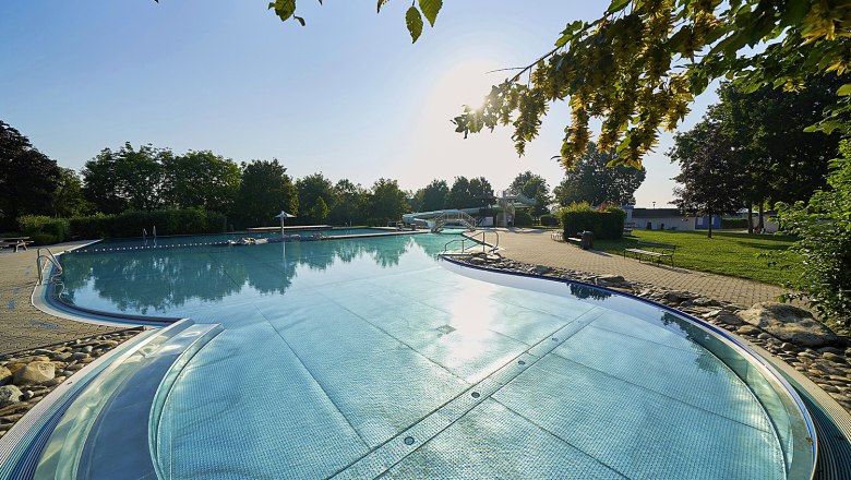 Absdorf outdoor pool, © Philipp Monihart An outdoor pool with clear water, surrounded by trees and a sunny sky.