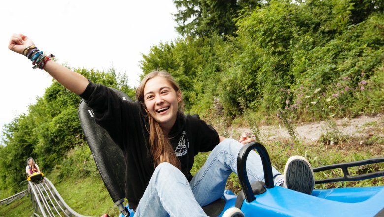 Eibl-Jet, © DorisSchwarzKoenig.at A smiling person rides on a summer toboggan run, surrounded by green nature.