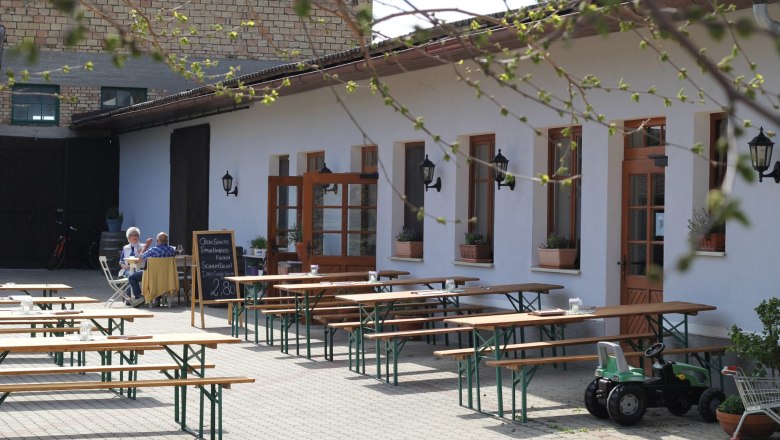 Buschenschank Demmer courtyard, © Thomas Norek Inner courtyard of a Buschenschank (typical tavern) with empty wooden benches and a table, two people sitting at a table, a toy tractor standing next to it.