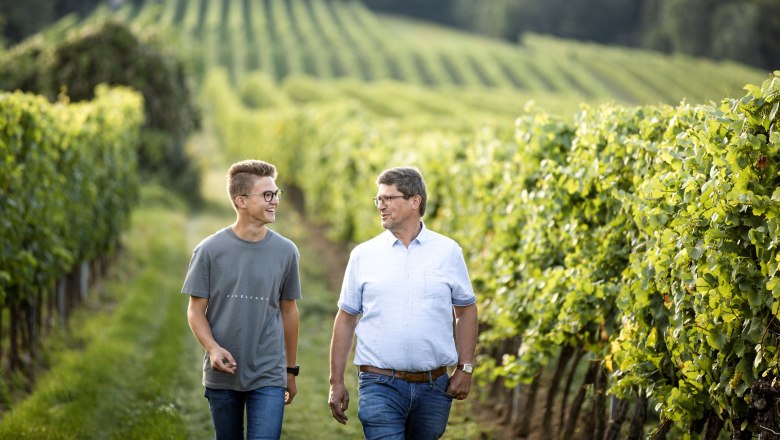 Wine tavern Oberschil, © Astrid Bartl Two men walk through a vineyard smiling.