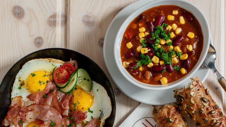 Hot snacks., © Koll GmbH Various hot snacks on a table, including sandwiches, fried eggs with bacon, soup and rolls.