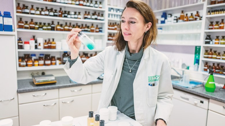 World of STYX- Laboratory, © Styx Naturkosmetic GmbH A woman in a white lab coat holds a test tube with blue liquid in a laboratory.