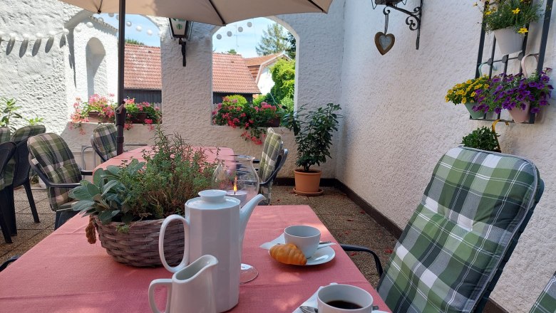 TDR-Pension Welserhof, © Bartfai Cozy outdoor area with laid table, coffee cups and pastries, surrounded by flowers and plants.