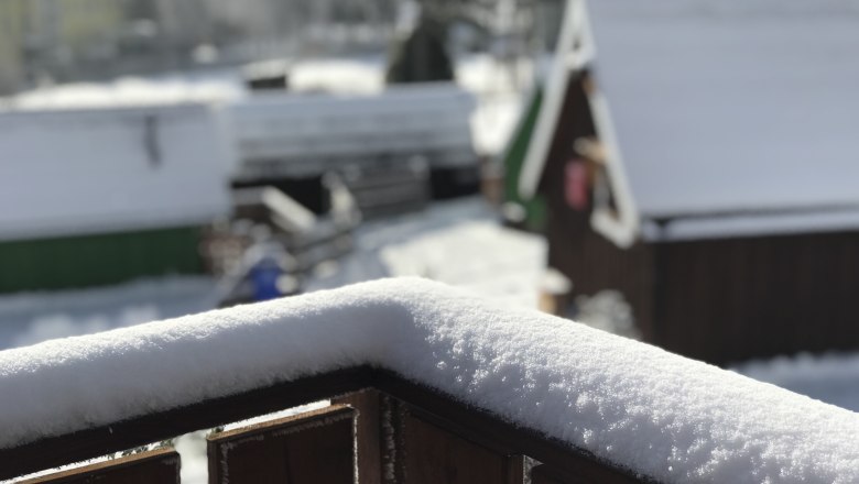 Glamping Park in winter, © Glamping-Park Mönichkirchen OG Snow-covered wooden beams in the foreground, blurred huts in the background.