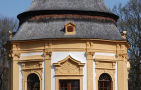 Garden pavilion, © Gemeinde Obersiebenbrunn Baroque garden pavilion with yellow decorations and a gray roof against a blue sky.