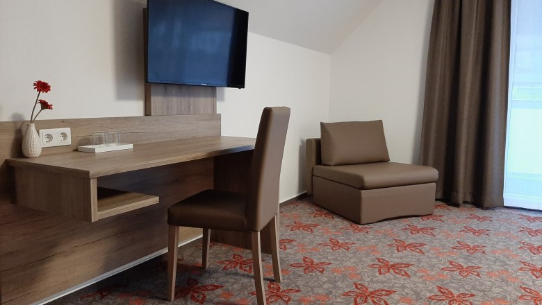 Double room, © Gerhard Auer Hotel room with desk, chair, TV and armchair.