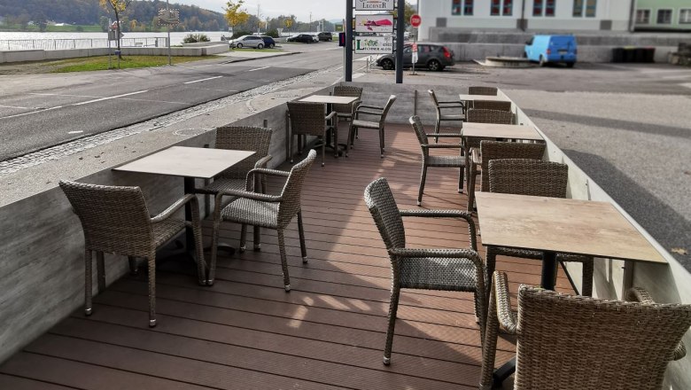 Cafe Lechner outdoor area, © Bäckerei Lechner Outside area of a café with empty tables and chairs, next to a street and a sign saying 'ADEG'.